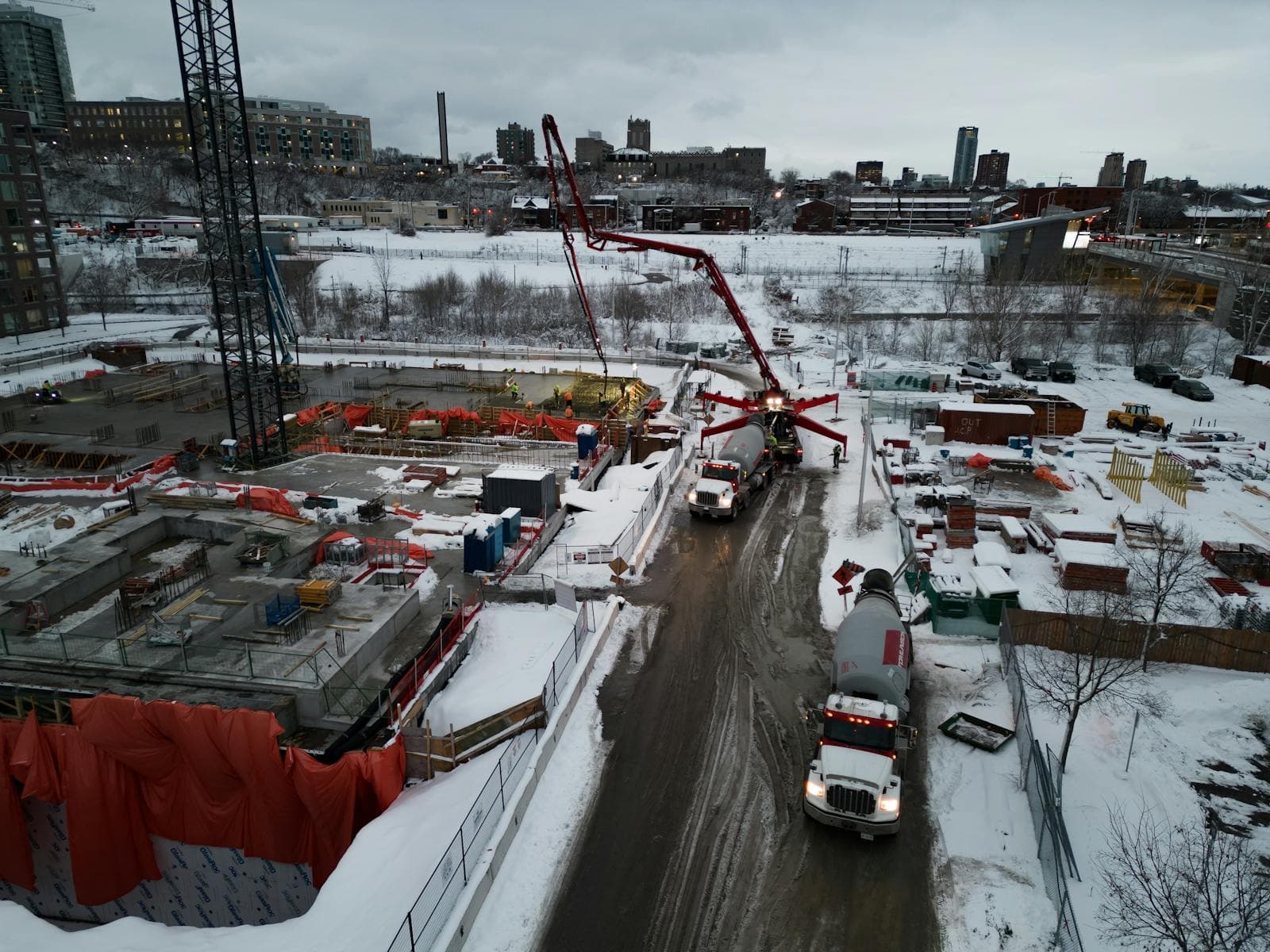 Aerial view of a snow-covered construction site with trucks and cranes in Ottawa, Canada.