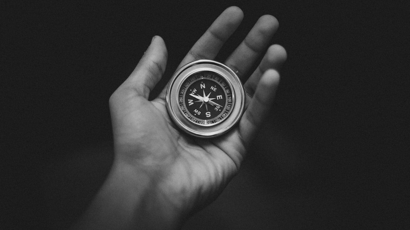 Black and white image of a hand holding a compass, conveying direction and exploration.