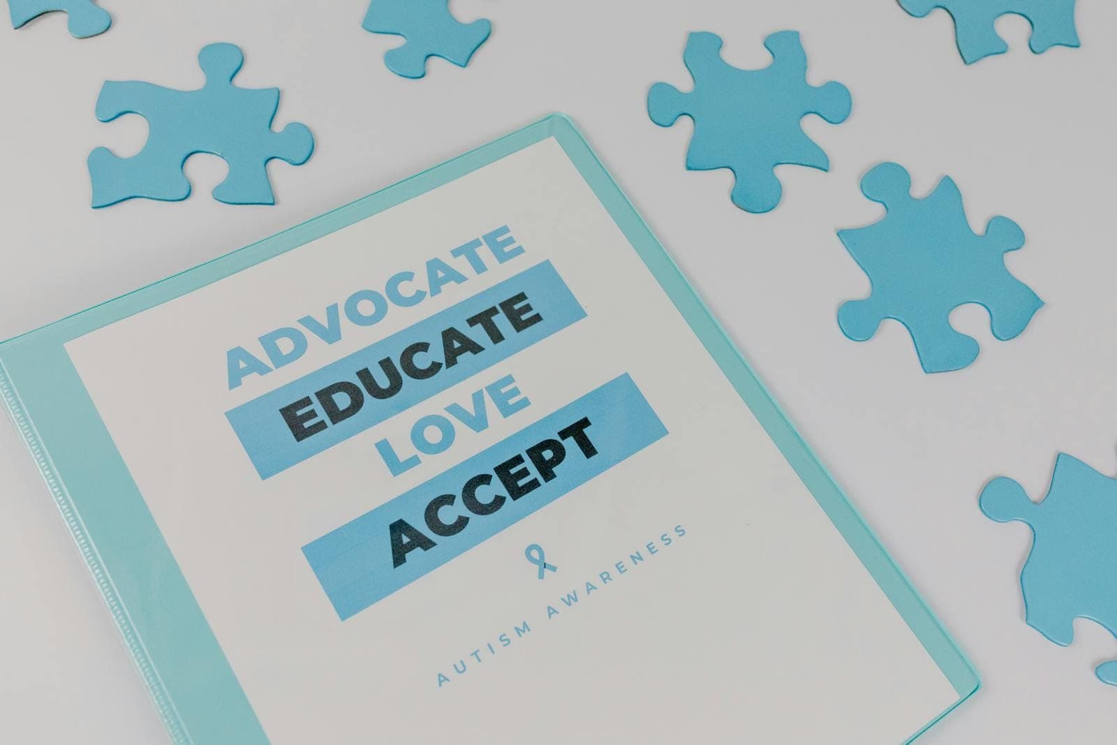 Binder with advocacy message amidst puzzle pieces for autism awareness.