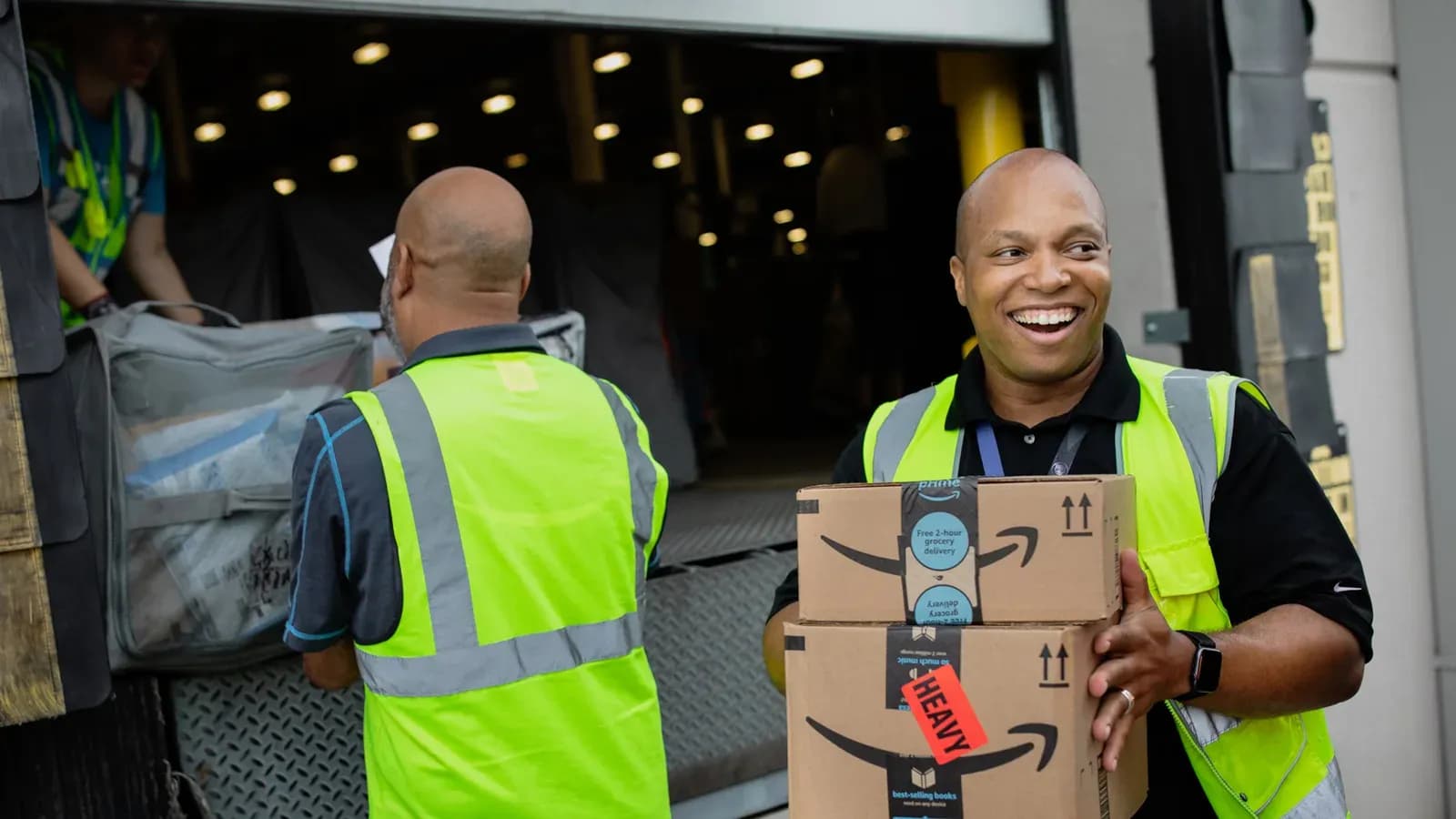 Two delivery workers in high visibility vests loading Amazon parcels at a delivery station