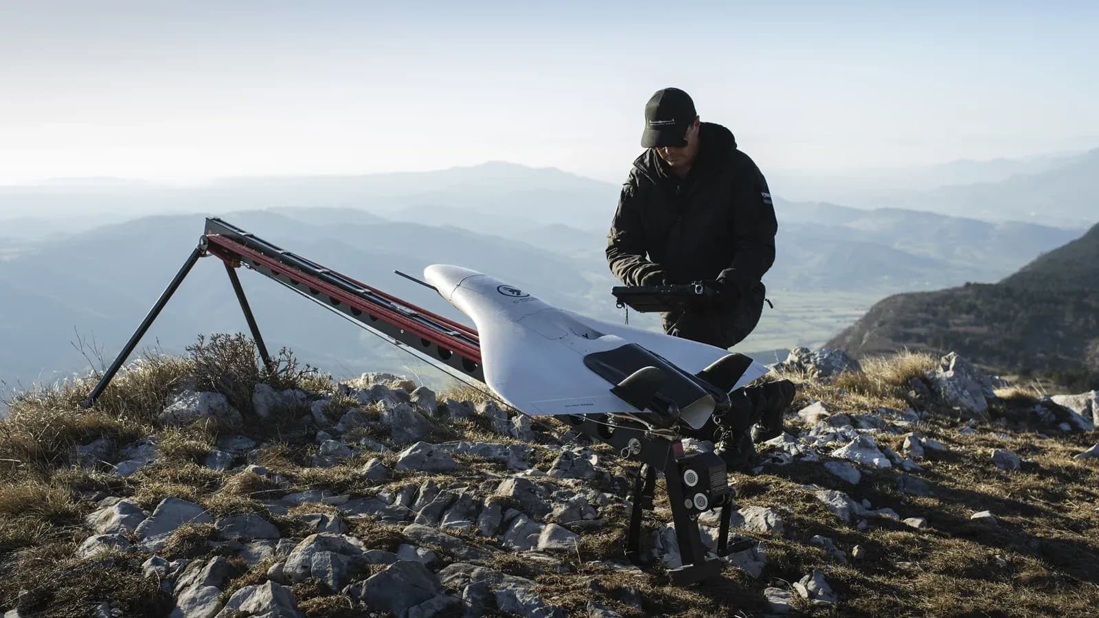 A C-Astral uncrewed aircraft on a catapult launcher on a mountain ridge, with an operator at a handheld control unit.