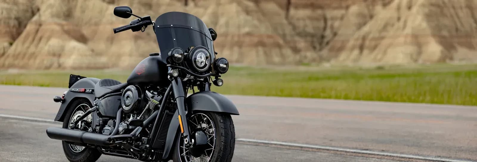 A blacked-out Harley-Davidson touring motorcycle parked on a desert highway with badlands rock formations in the background