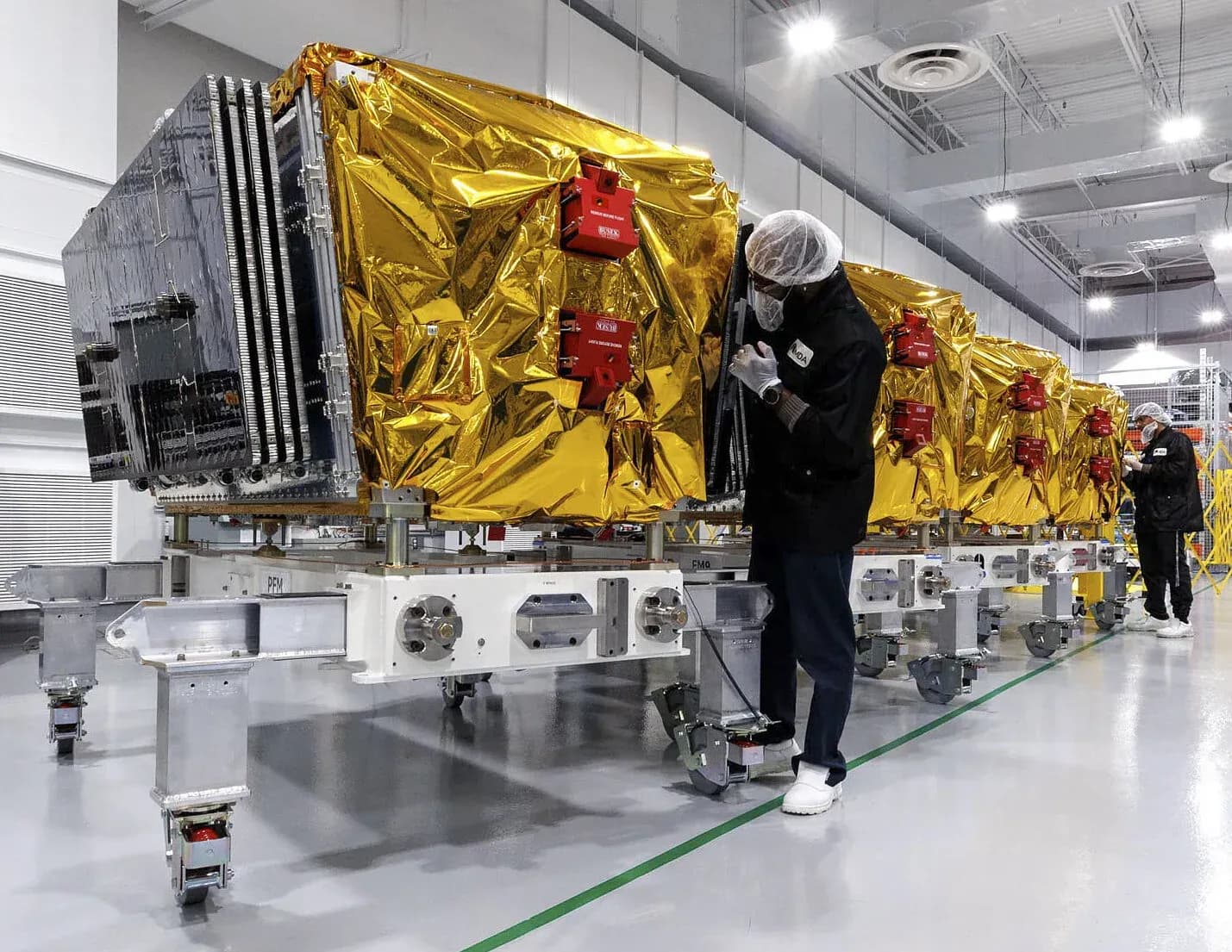 MDA Space satellites with gold thermal shielding under assembly in a cleanroom with technicians