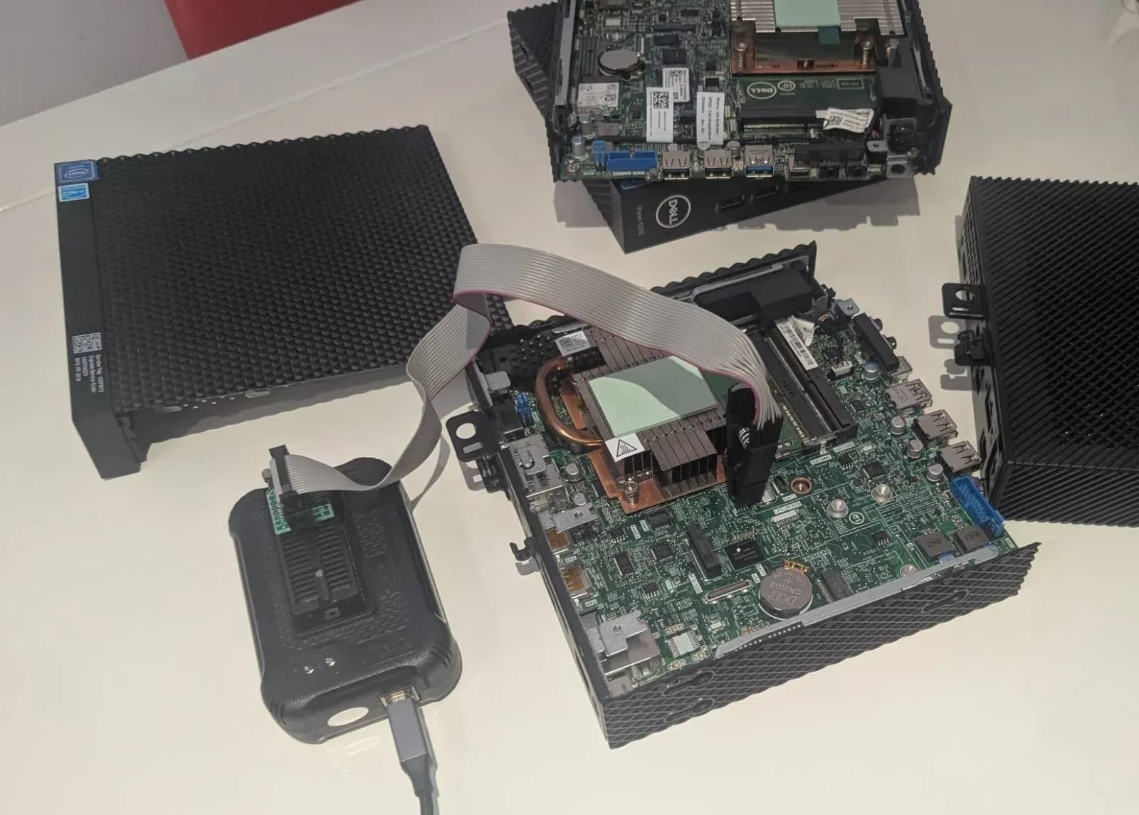 A disassembled Dell computer on a workbench with a test clip attached to its mainboard and a chip programmer alongside