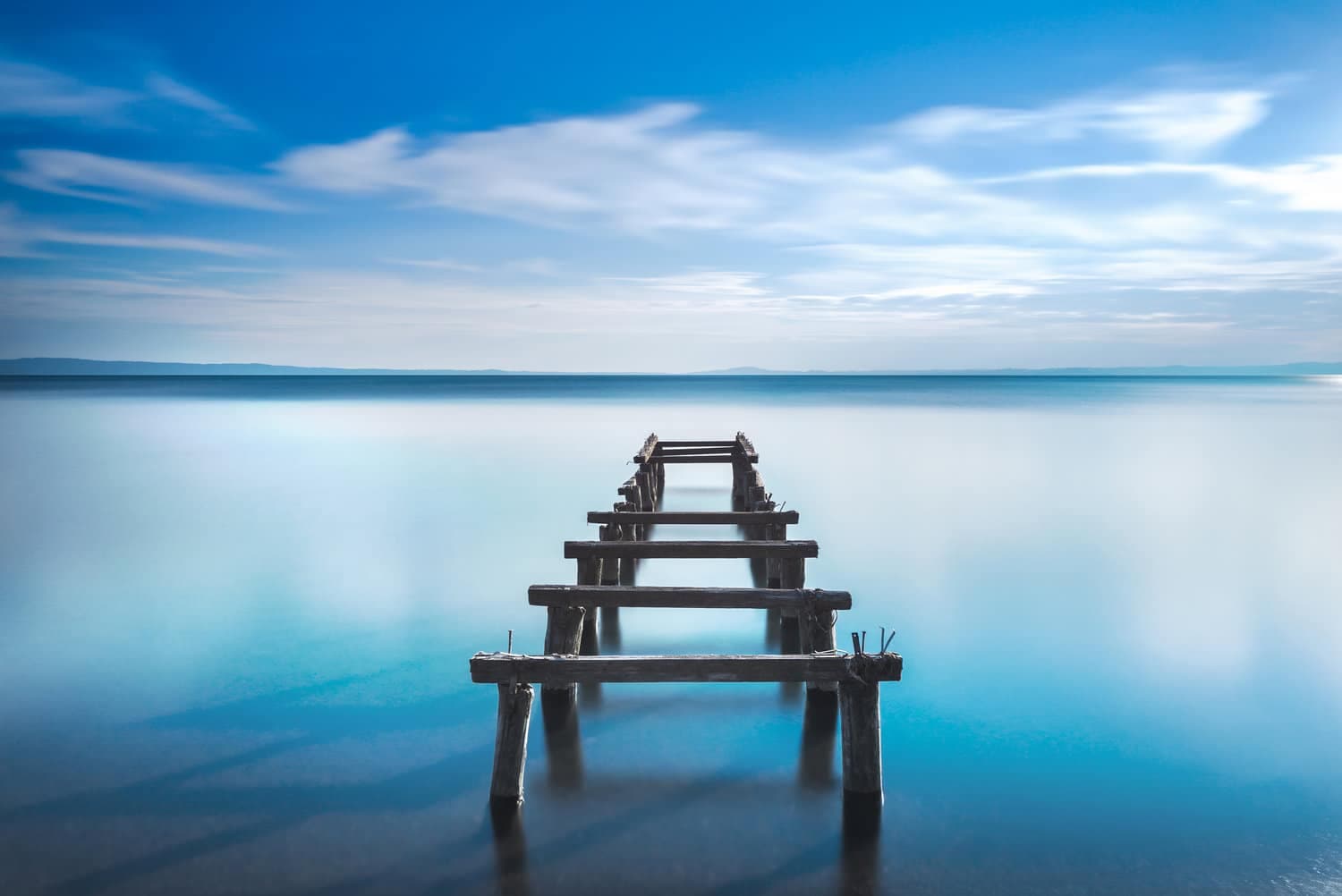 Wooden pier or jetty remains on a blue lake. Long Exposure.