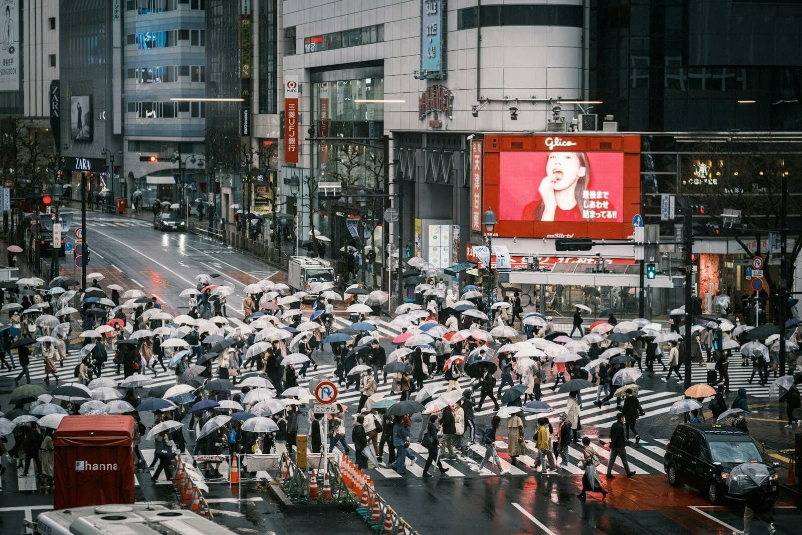 A bustling Tokyo street scene with pedestrians crossing in the rain under umbrellas.