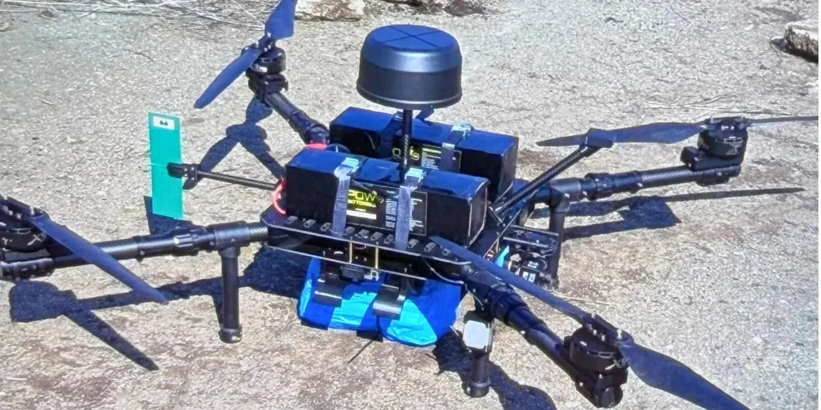 A multirotor delivery drone on rocky ground with a blood plasma payload strapped underneath, before a flight in Ukraine.