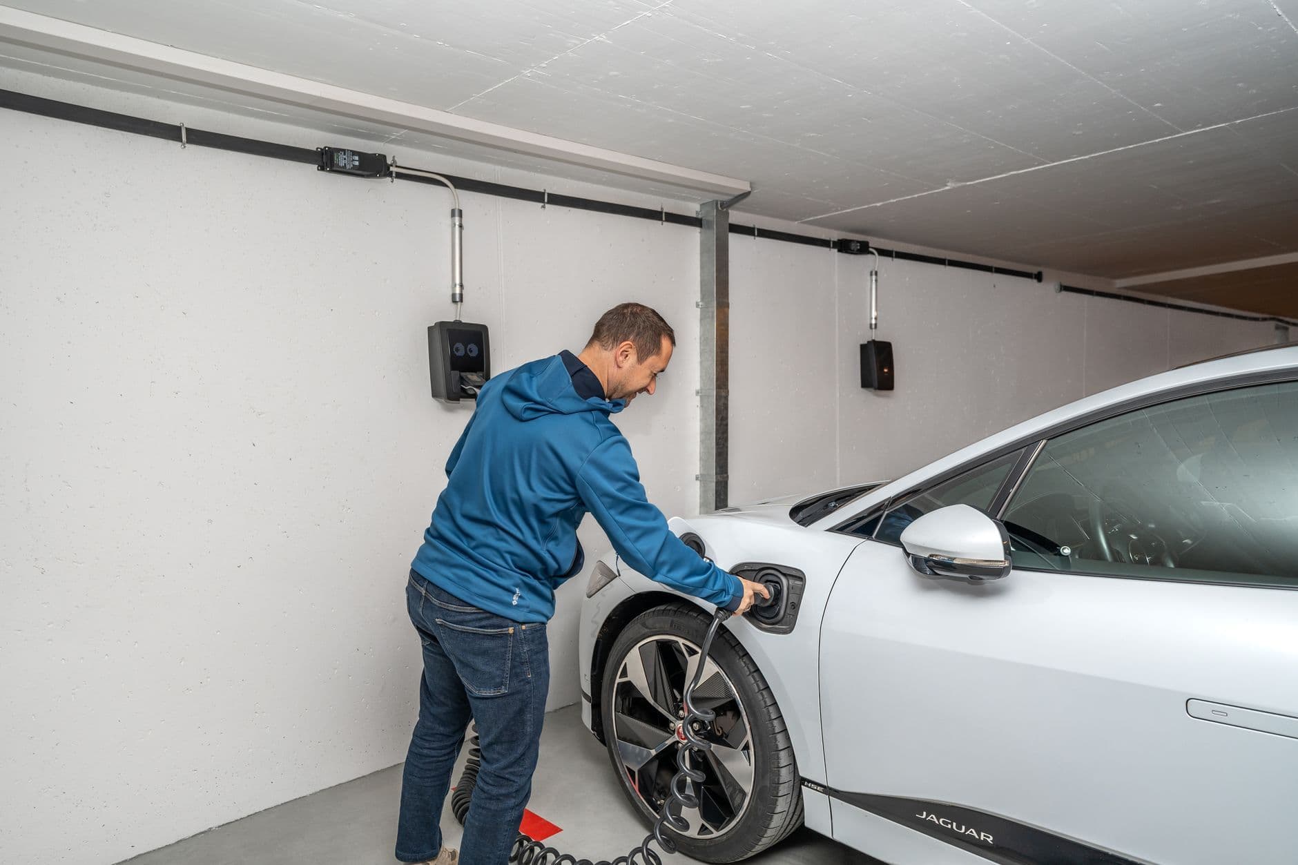 A man plugs an electric car into a wall-mounted charger in a home garage