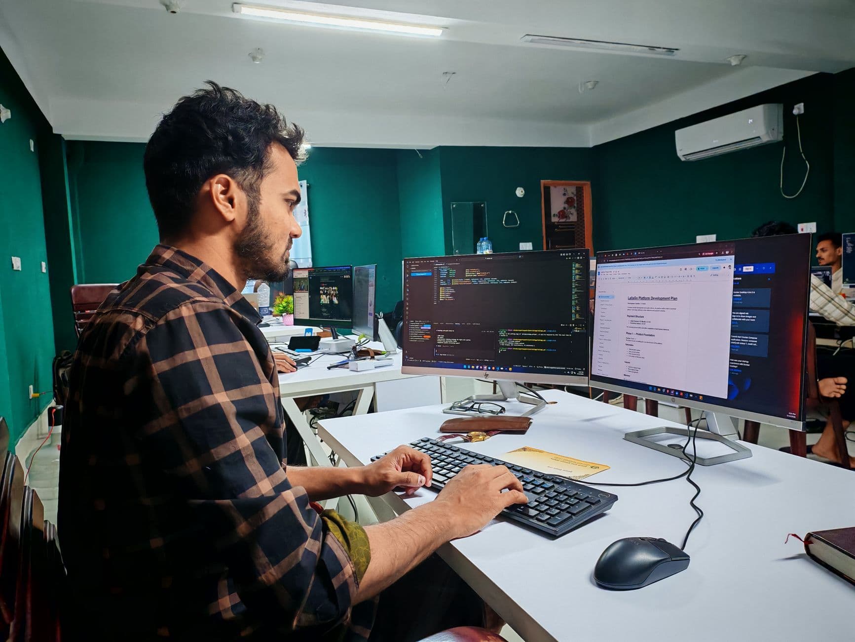 A software developer working at a dual-monitor desk in a modern office