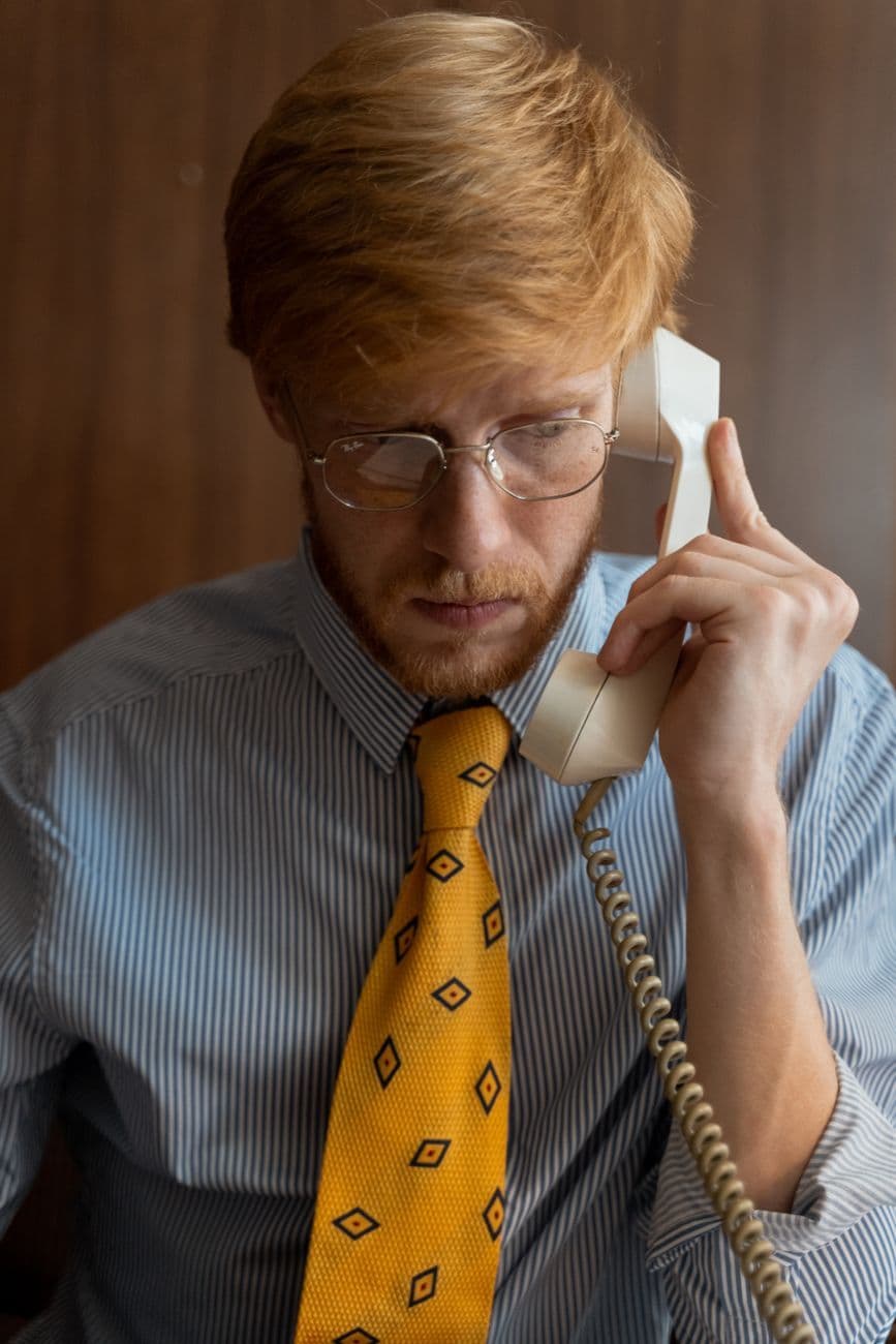 Businessman with a yellow tie conversing on a vintage landline phone in an office.
