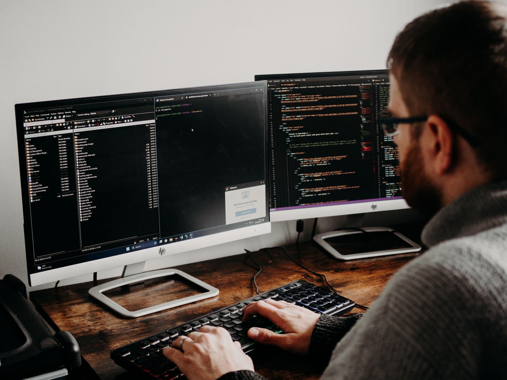 A software developer types at a desk with code open on two monitors