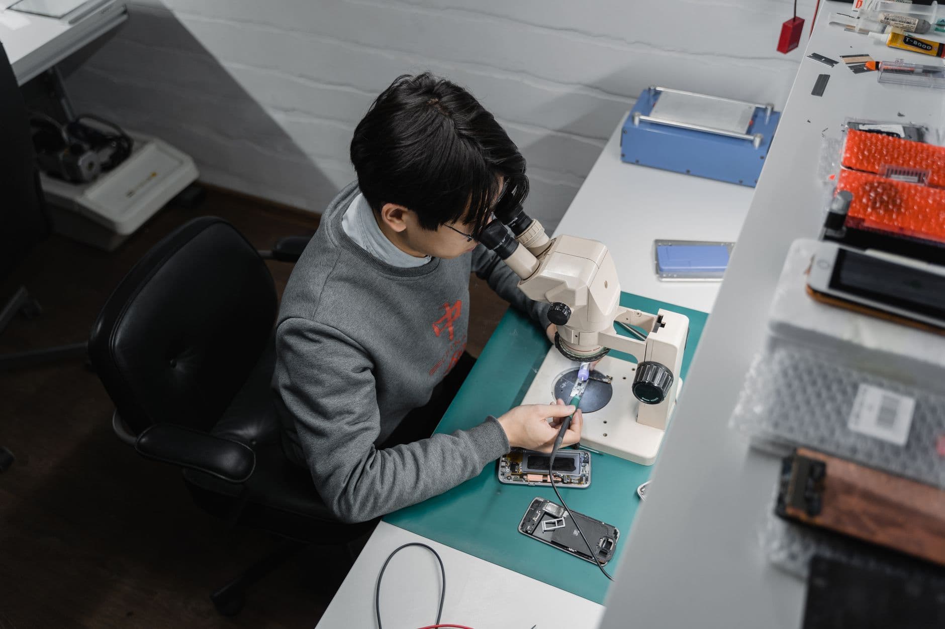 A technician repairs a smartphone under a microscope at a workbench.