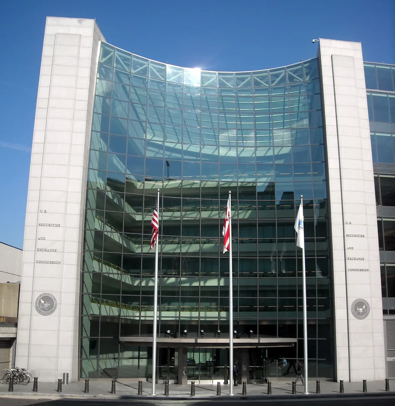 Exterior of the U.S. Securities and Exchange Commission headquarters in Washington DC, a glass and stone facade with the agency name engraved on the pillars and flags out front