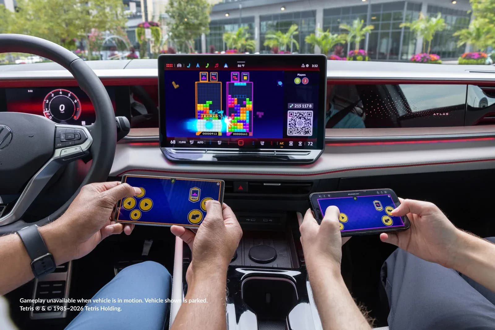 Two passengers play Tetris on the infotainment screen of a parked 2027 Volkswagen Atlas using their smartphones as controllers