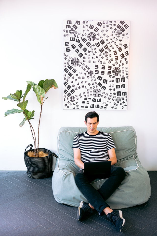 Millennial man sitting on a cozy cushin while working on his laptop